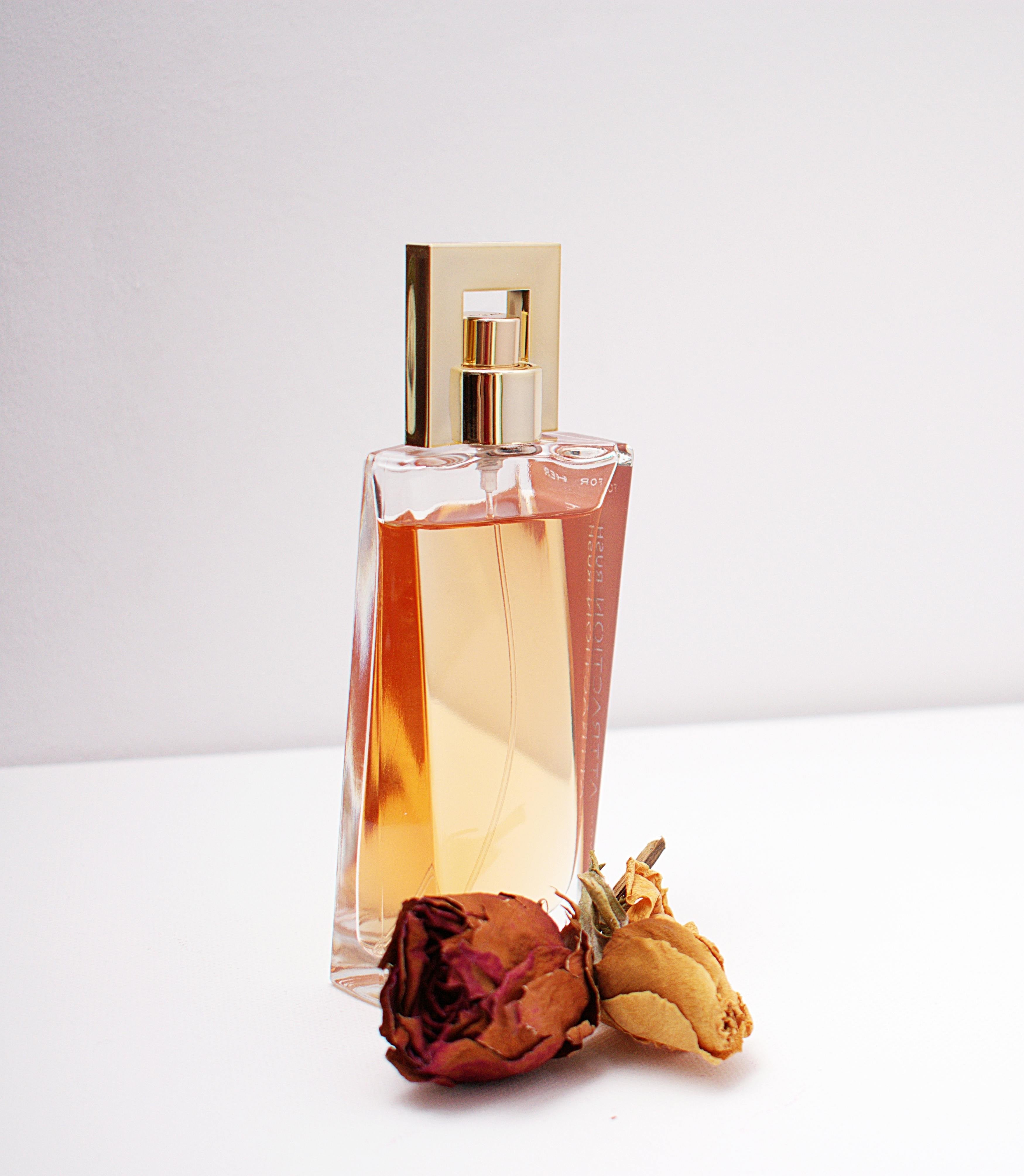 a tall glass bottle with amber liquid and a dried rose next to it